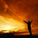 Enlightenment man standing with arms spread before a beautiful sunset.